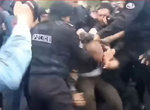 Полицейский ударяет кулаком по голове протестующего